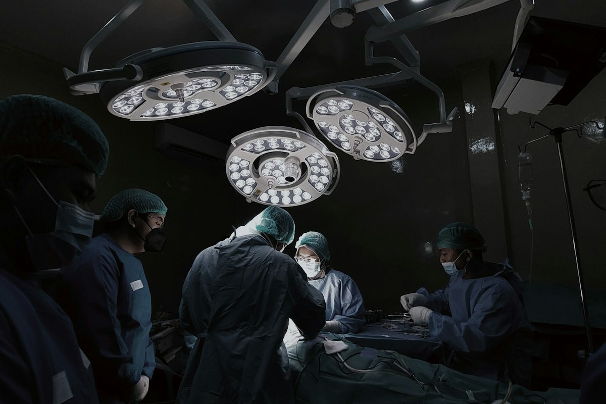 A surgical team in masks and gowns operating beneath bright theatre lights