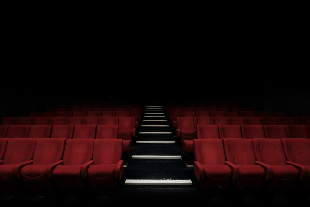 Rows of empty red cinema seats either side of lit steps in a dark auditorium