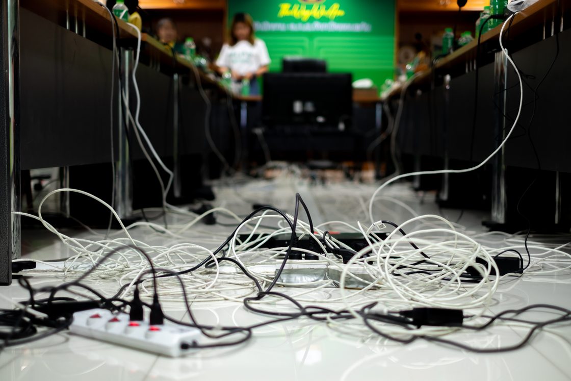 Kabel dan kabel ekstensi kusut di lantai di antara dua deretan meja.