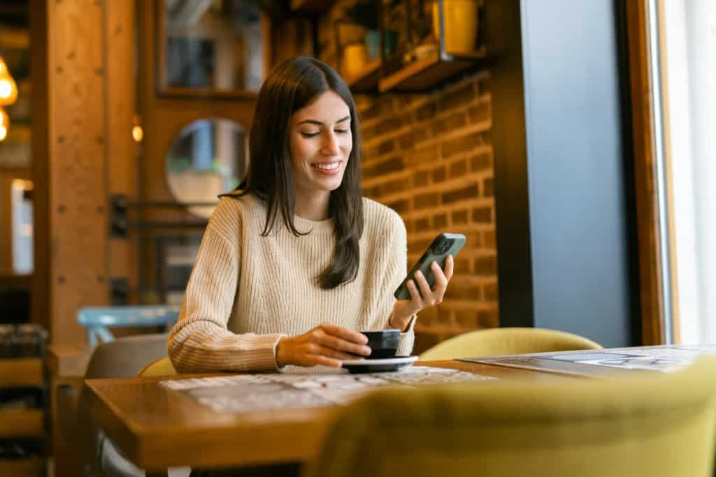 Kvinde nyder en kaffe mens hun smiler på sin telefon på en café.
