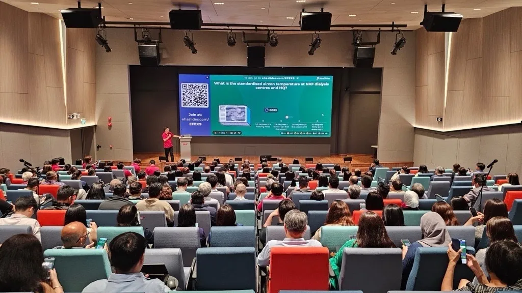 誰かが講堂で聴衆の前でAhaSlidesを使ってプレゼンテーションを行っている。