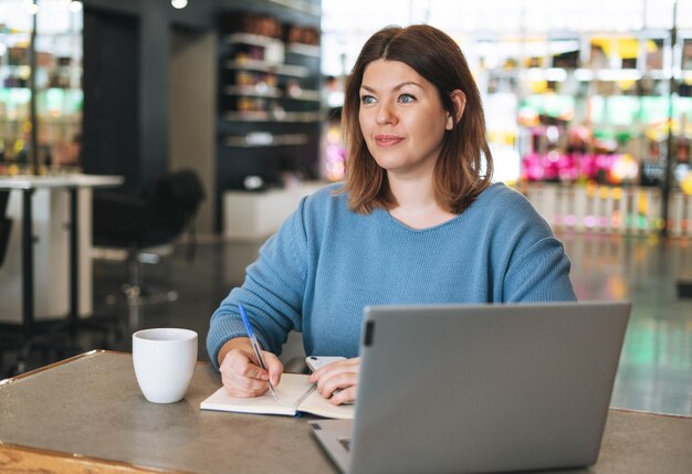 Une femme prend des notes tout en apprenant sur un ordinateur portable dans un café
