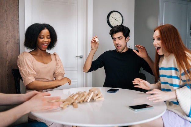 Friends playing Jenga block game together at table laughing