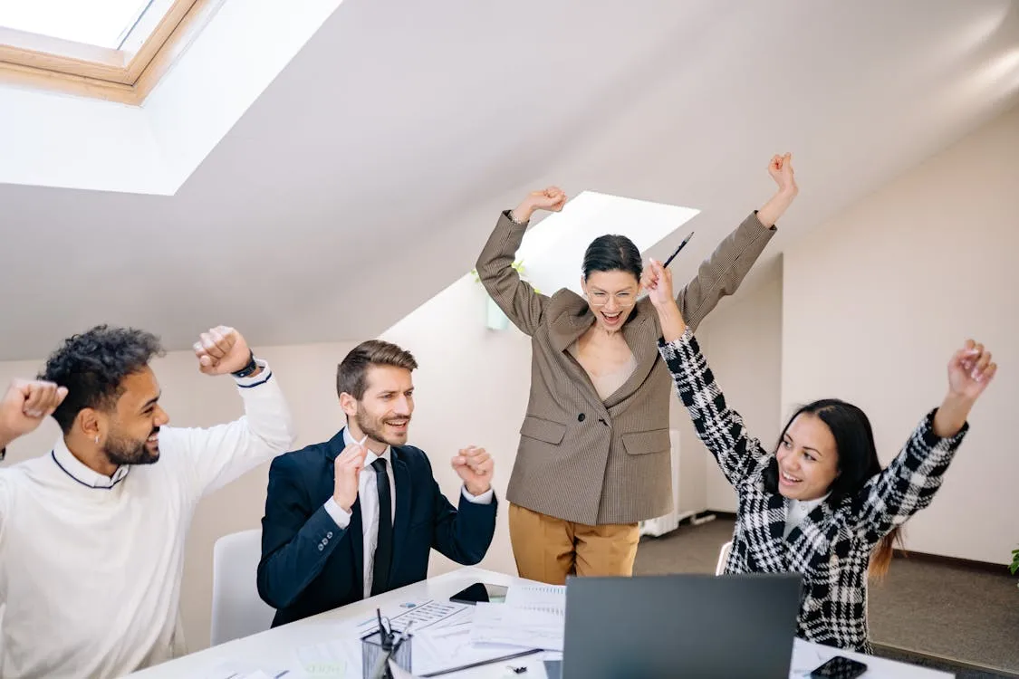 Excited team celebrating together with arms raised during an office ceremony