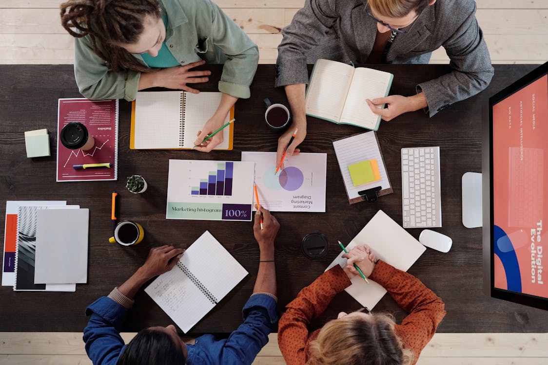 Overhead view of colleagues collaborating with notebooks and charts at a meeting table