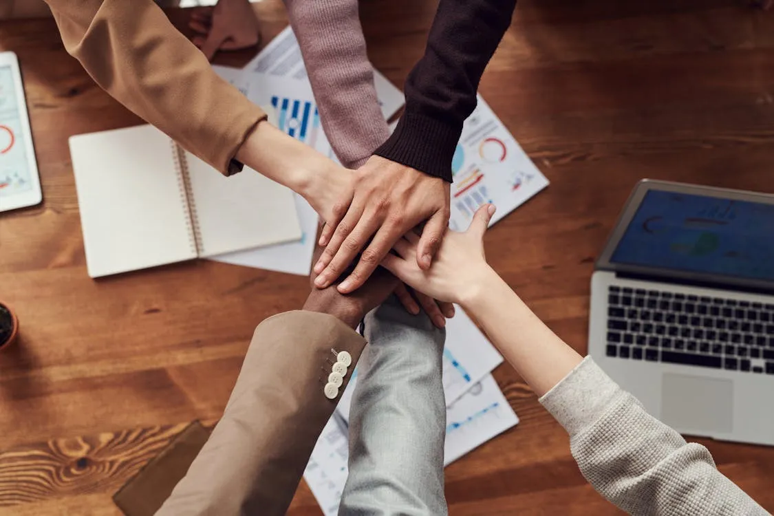 Team putting hands together over a table with documents and laptop showing unity and connection