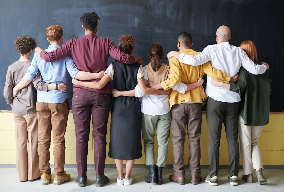Diverse group of colleagues standing arm in arm facing a blackboard showing team connection and trust