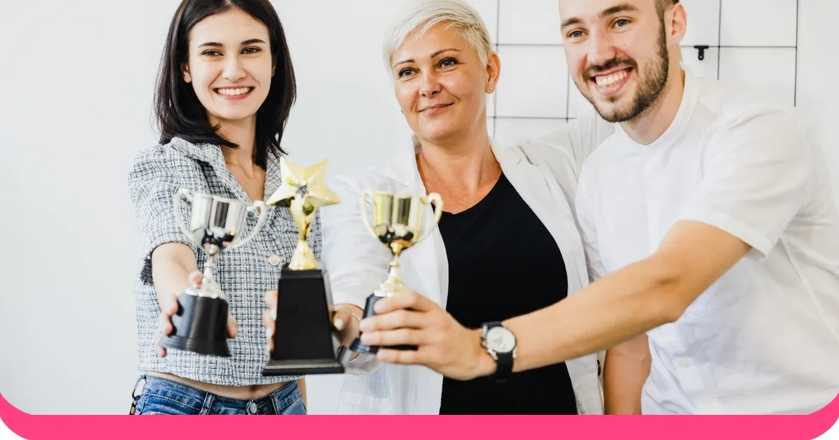Trzech uśmiechniętych kolegów trzymających małe złote trofea w jasnym biurze