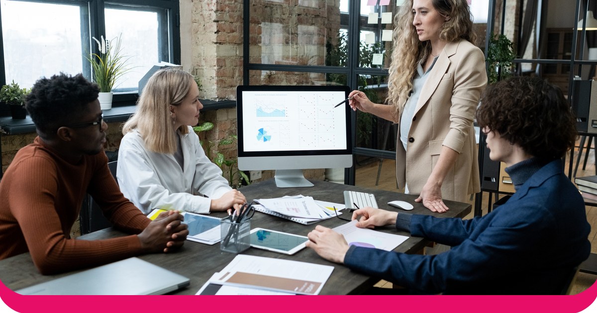 A woman presenting charts on a monitor to three colleagues around a meeting table