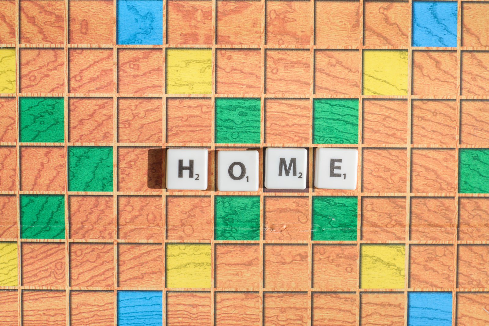 Scrabble board na may mga tile na gawa sa kahoy na nagbabaybay ng salitang HOME sa mga may kulay na bonus squares