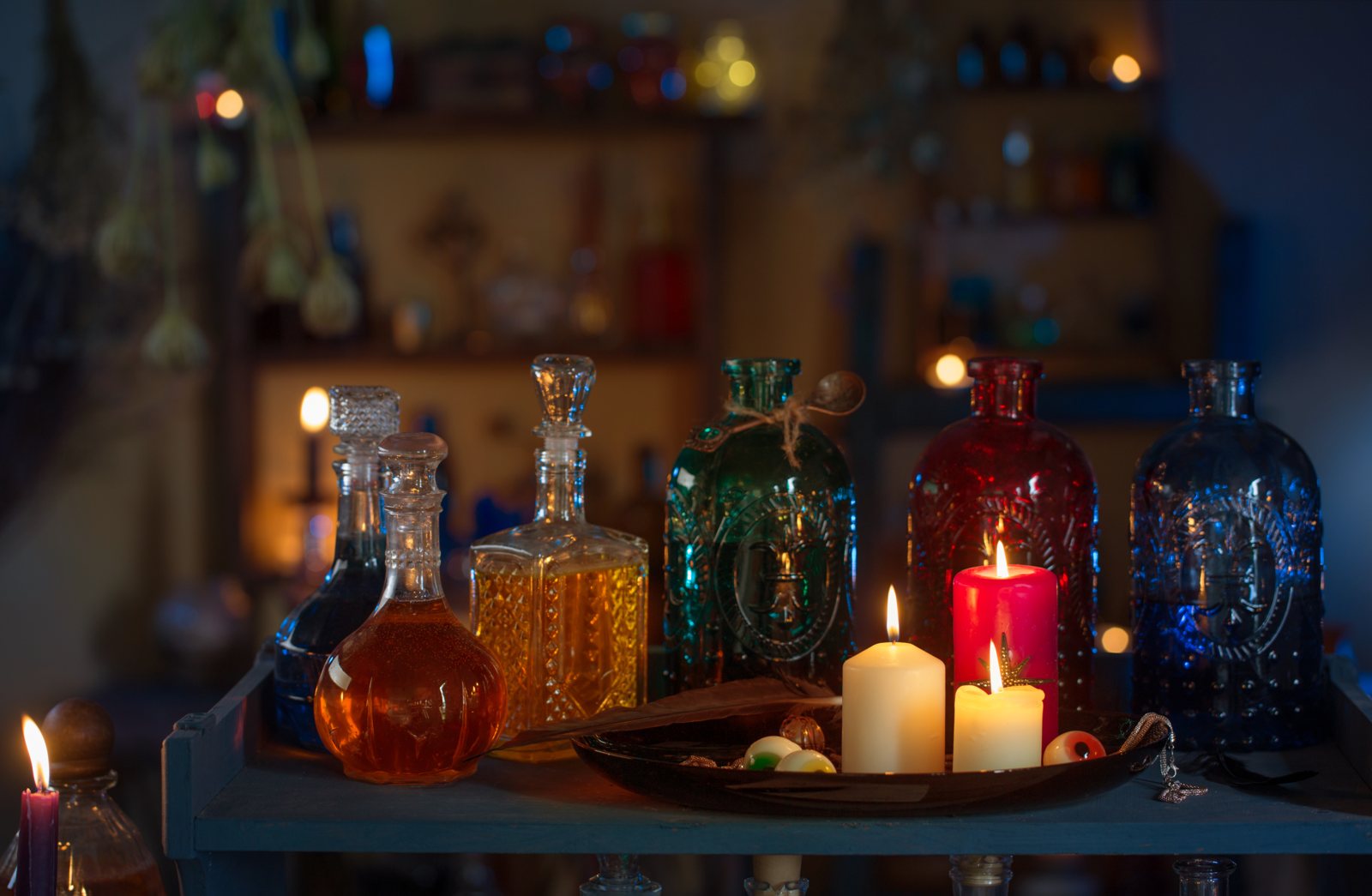 Glass potion bottles in different colours on a shelf beside lit candles