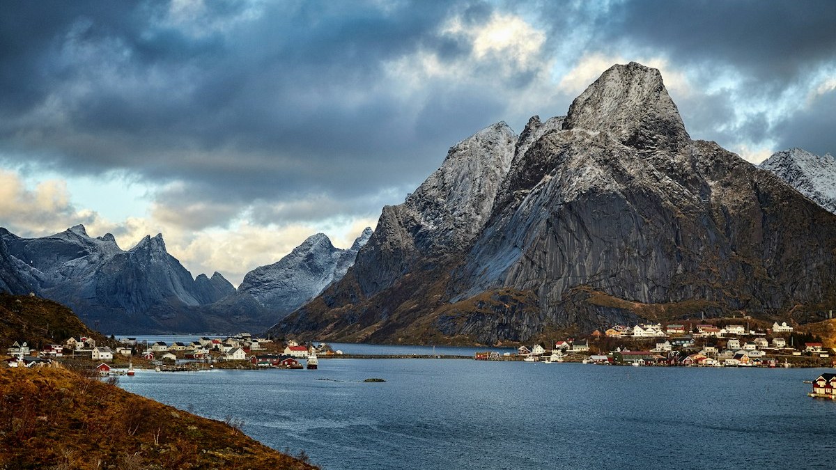 A small fishing village below a steep rocky mountain under stormy clouds