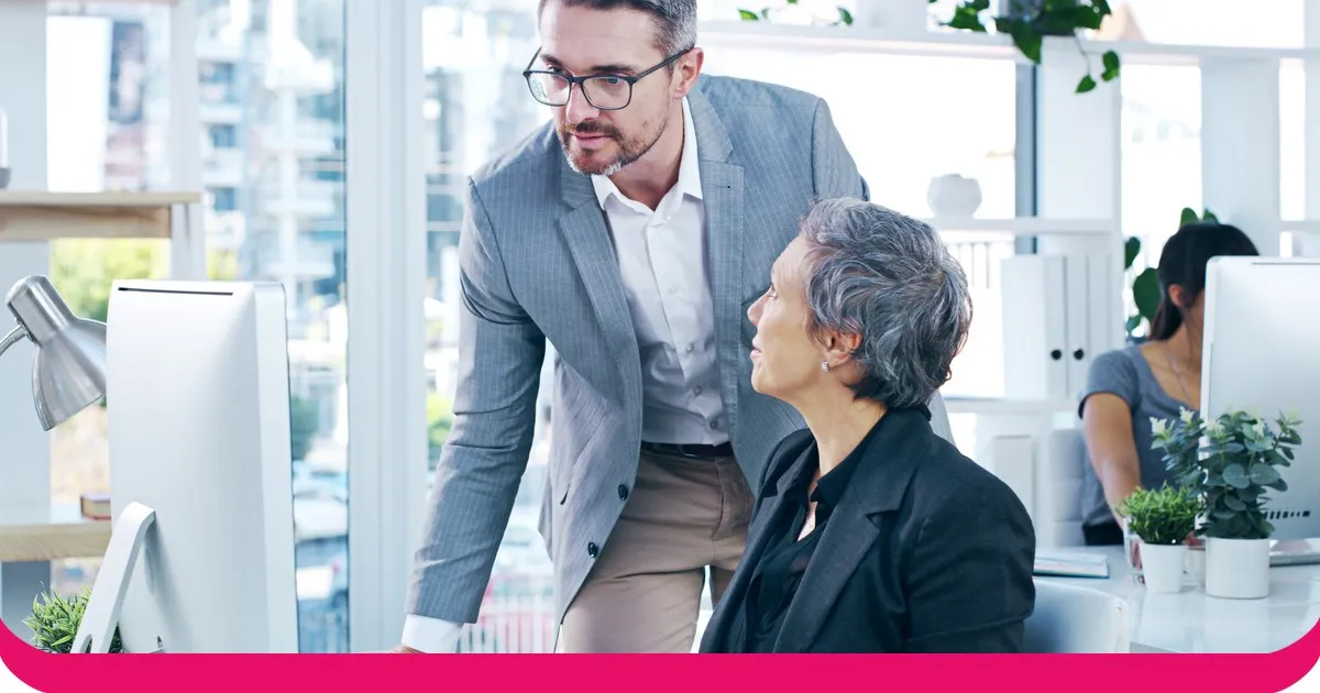 A sales manager sits beside a colleague at a screen, giving coaching feedback