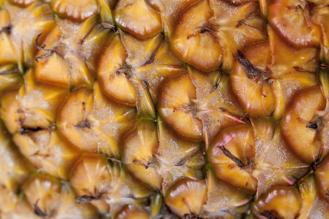 Extreme close-up of the rough, diamond-patterned yellow skin of a pineapple
