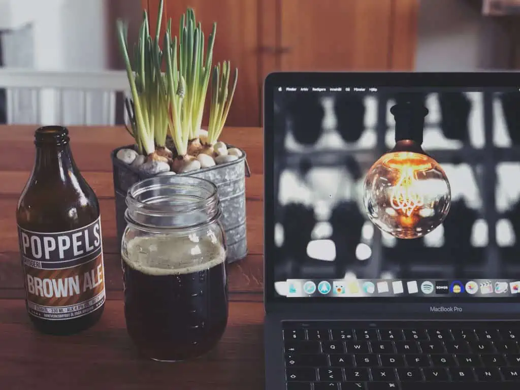 O sticlă de bere și un laptop deschis pe o masă.