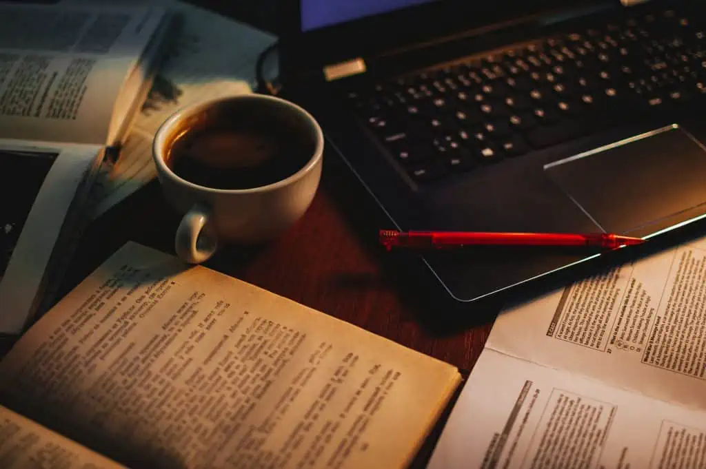 Imatge de llibres, papers, un ordinador portàtil, un cafè i un bolígraf.