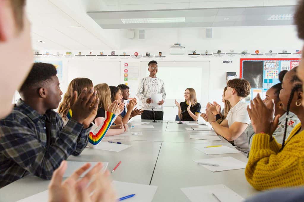 Lernantoj gratulas la parolanton post sukcesa studenta debato en la klaso.