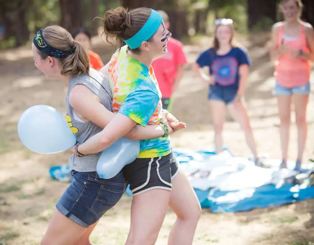 Две девушки играют в командные воздушные шары во время 5-минутного тимбилдинга в лесу.