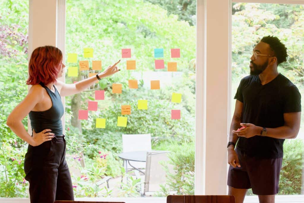 Two people having a brainstorming session with post-its on a window.