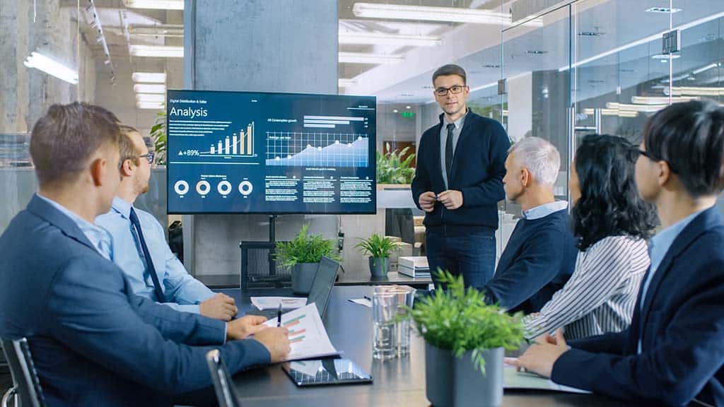 Man showing a presentation with graphs to a boardroom full of people