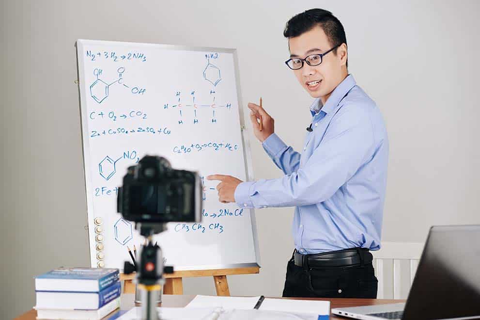 Professor universitário explicando fórmulas químicas no shiteboard durante a aula online